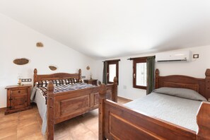 Une chambre à coucher avec un lit en bois, une table de chevet, une commode, une fenêtre avec des rideaux et un appareil de climatisation.