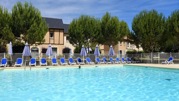 Una piscina con sillas y sombrillas azules, rodeada de árboles y edificios.
