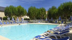 Piscina con tumbonas y sombrillas, rodeada de árboles y una valla.