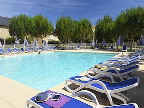 A swimming pool with sun loungers and umbrellas, surrounded by trees and a fence.