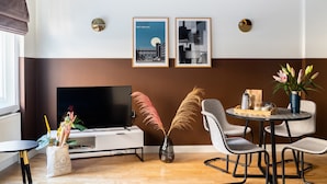 Una sala de estar moderna con un televisor de pantalla plana, una mesa de centro con un jarrón de flores y dos carteles enmarcados en la pared.