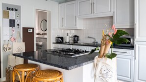 Una cocina moderna con armarios blancos, encimera de granito, estufa a gas y taburetes de mimbre.