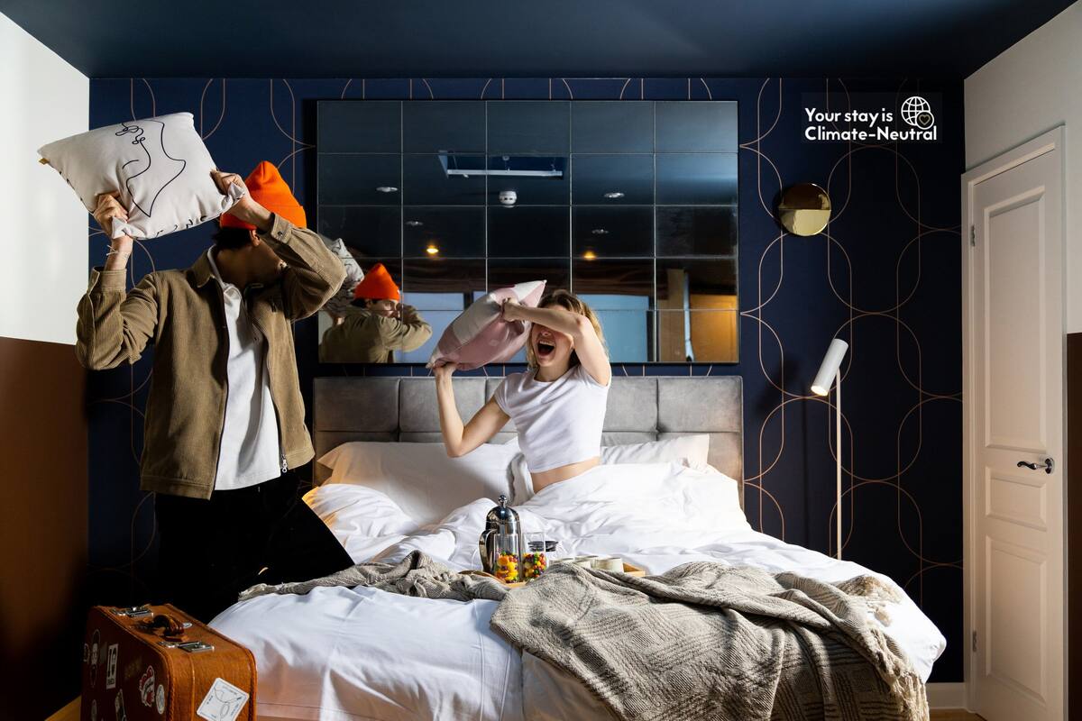 Habitación de hotel con una cama, una maleta y una pared con un globo terráqueo y texto.