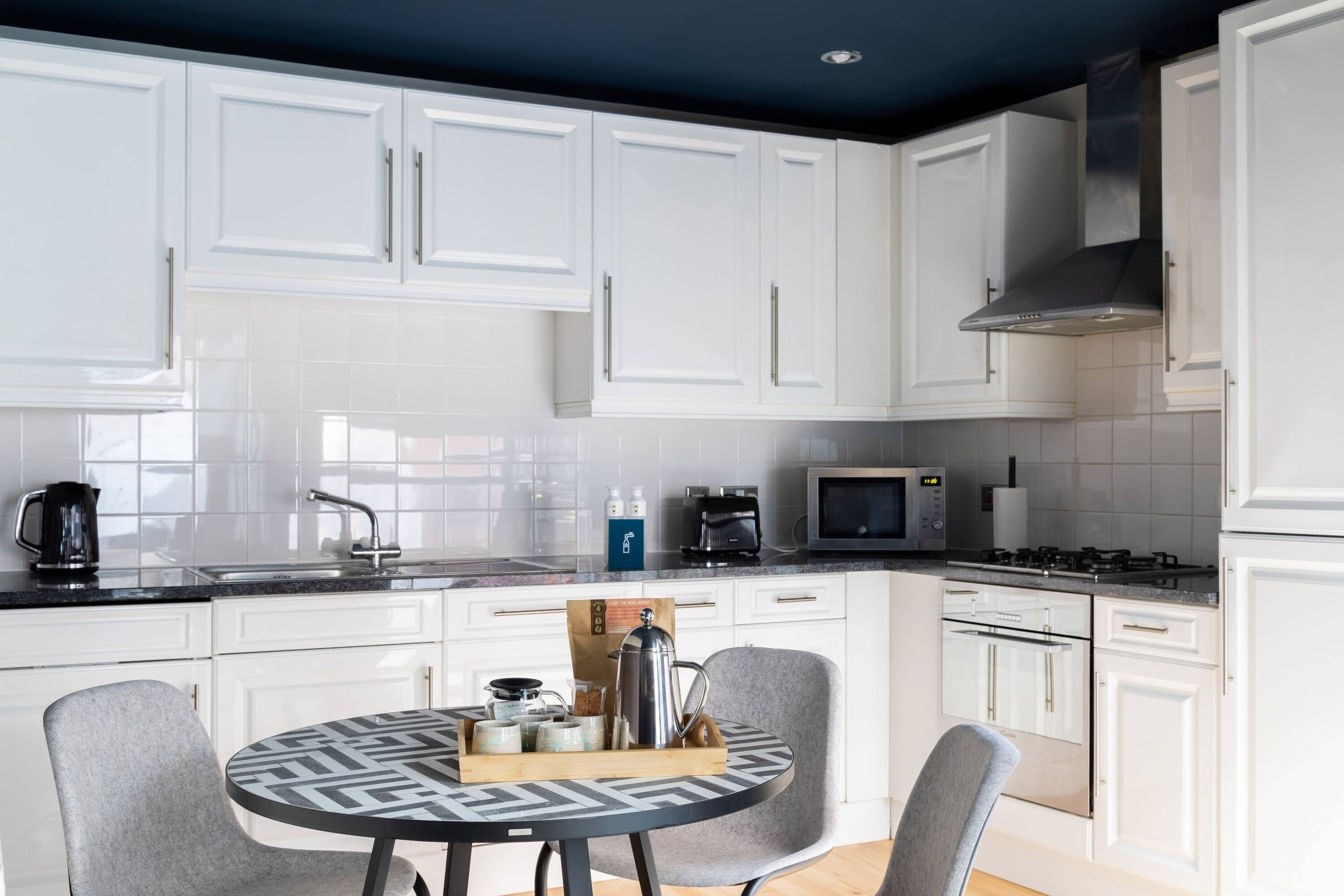 Een moderne keuken met witte kasten, een ronde tafel met stoelen, een fornuis en een magnetron.