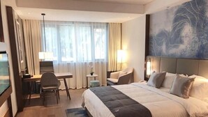 Ein Hotelzimmer mit Bett, Schreibtisch, Stuhl, einem kleinen Tisch und einem Fenster mit Vorhängen.