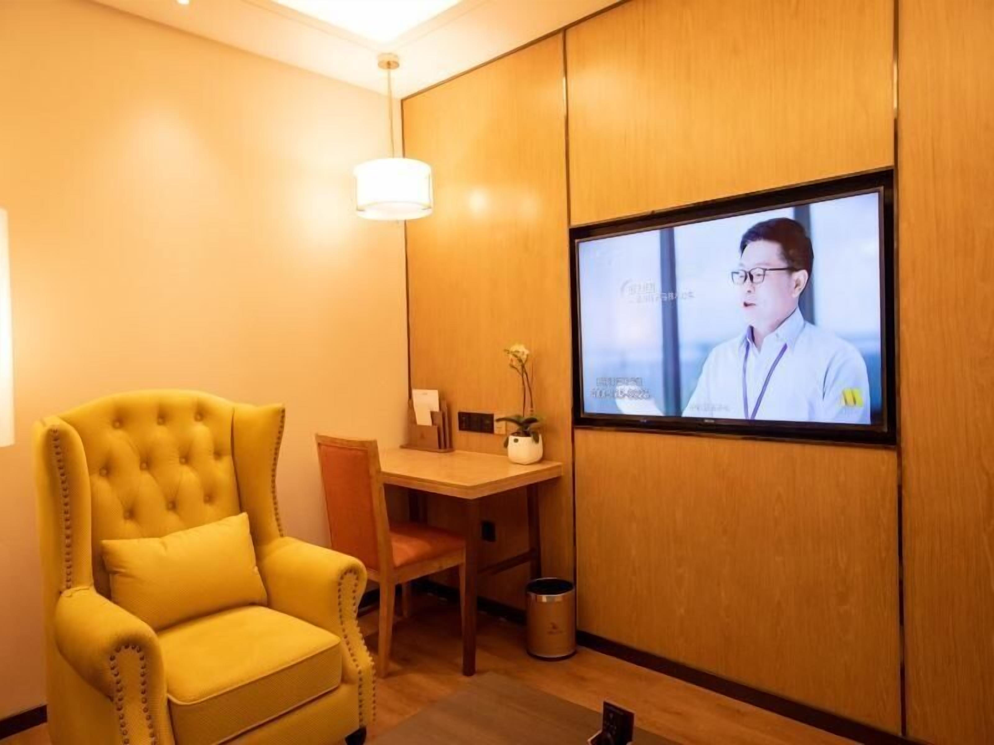Une pièce avec un fauteuil jaune, un bureau en bois, une télévision et une petite poubelle.