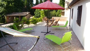 Un patio con poltrone verdi, un ombrellone rosso e un tavolo in mattoni.