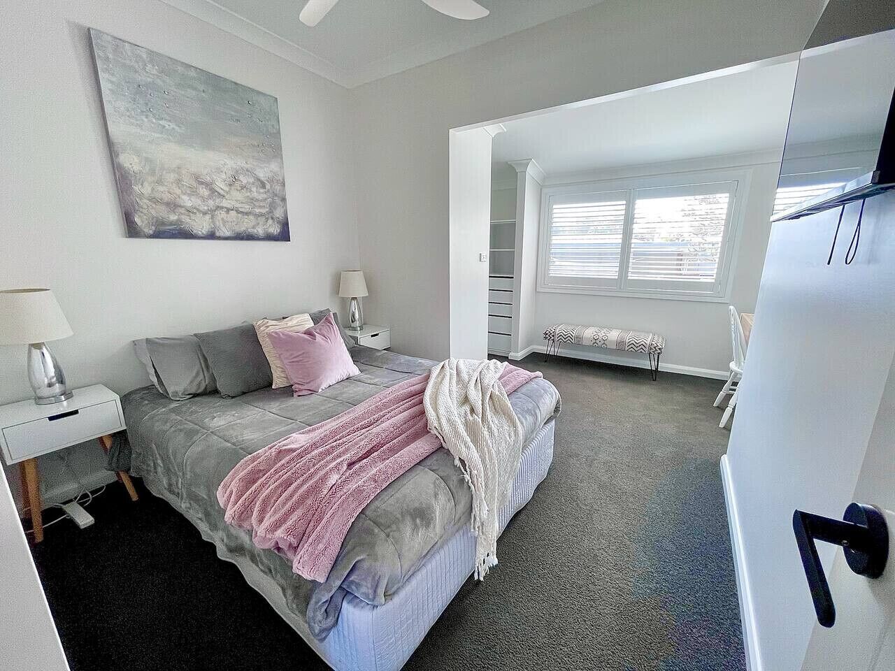 A bedroom with a bed, nightstands, a lamp, a window, and a door.