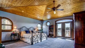 A bedroom with a wooden ceiling, a bed with a metal frame, a nightstand, a lamp, and a bookshelf. - Unique cottage (Alberta)