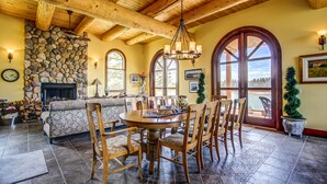 A rustic dining area with a stone fireplace, wooden ceiling beams, and large arched windows. - Unique cottage (Alberta)