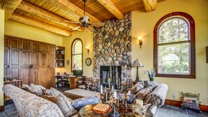 A cozy living room with a stone fireplace, wooden ceiling beams, and large windows. - Unique cottage (Alberta)