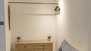 Ett sovrum med en byrå i trä, två små krukväxter, en hängande lampa och en mönstrad kudde.