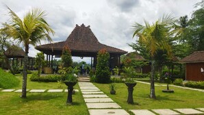 Ein pavillon im traditionellen Stil mit Ziegeldach, umgeben von gepflegtem Rasen und Palmen, der zu einem überdachten Sitzbereich führt.