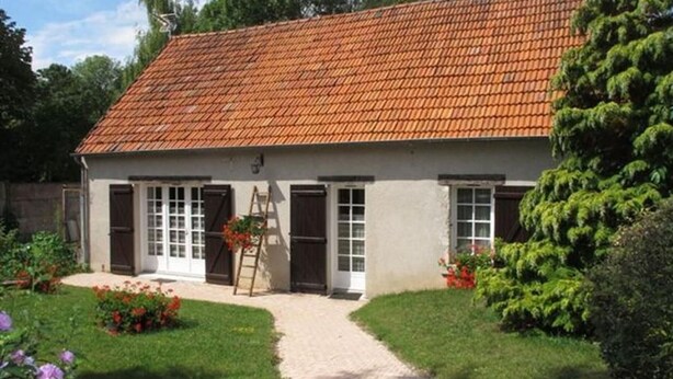 A two-story house with a tiled roof, a front porch, and a garden with flowers and a tree.