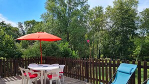 A wooden deck with a table and chairs, a red umbrella, and a blue lounge chair.