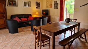 A cozy living room with a black sofa, a wooden dining table, and a TV.