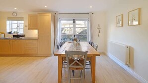 A kitchen with wooden cabinets, a dining table with chairs, a window with curtains, and a radiator. - Townhouse with Views of Wells Cathedral (Wells)