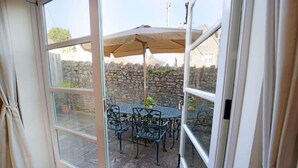 A patio with a round table and chairs, an umbrella, and a stone wall in the background. - Townhouse with Views of Wells Cathedral (Wells)