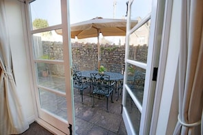 A glass door leading to an outdoor patio with a round table and chairs, an umbrella, and a stone wall in the background. - Townhouse with Views of Wells Cathedral (Wells)