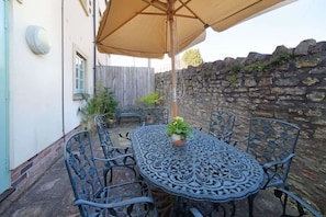 A patio with a round table and chairs, a potted plant, and a stone wall. - Townhouse with Views of Wells Cathedral (Wells)