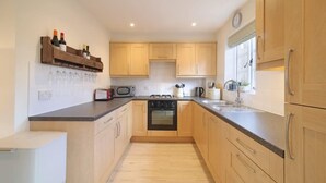 A modern kitchen with wooden cabinets, a built-in oven, a microwave, and a wine rack. - Townhouse with Views of Wells Cathedral (Wells)