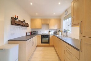 A modern kitchen with wooden cabinets, a built-in oven, a microwave, and a wine rack. - Townhouse with Views of Wells Cathedral (Wells)