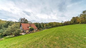 A house with a red roof, surrounded by a grassy field and trees. - Apartment in Marktrodach mit Sauna (Marktrodach)