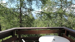 A wooden deck with a white table and chair, surrounded by dense forest. - Cozy Ski-In/Ski-Out Apartment with Fireplace, Sleeps 6, Balcony, Near Amenities (Les Orres)