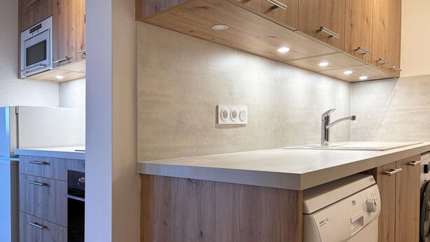 A modern kitchen with wooden cabinets, a built-in oven, a dishwasher, and a countertop with a sink. - Cozy Ski-In/Ski-Out Apartment with Fireplace, Sleeps 6, Balcony, Near Amenities (Les Orres)