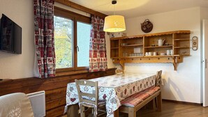 A cozy living room with a wooden bench, a table with a patterned tablecloth, and a hanging light fixture. - Cozy Ski-In/Ski-Out Apartment with Fireplace, Sleeps 6, Balcony, Near Amenities (Les Orres)