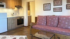 A compact living space with a kitchenette, a sofa with checkered upholstery, and a glass coffee table. - Cozy Ski-In/Ski-Out Apartment with Fireplace, Sleeps 6, Balcony, Near Amenities (Les Orres)