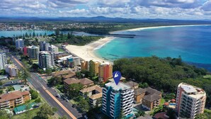 An aerial view of a coastal city with a beach, buildings, and a road.