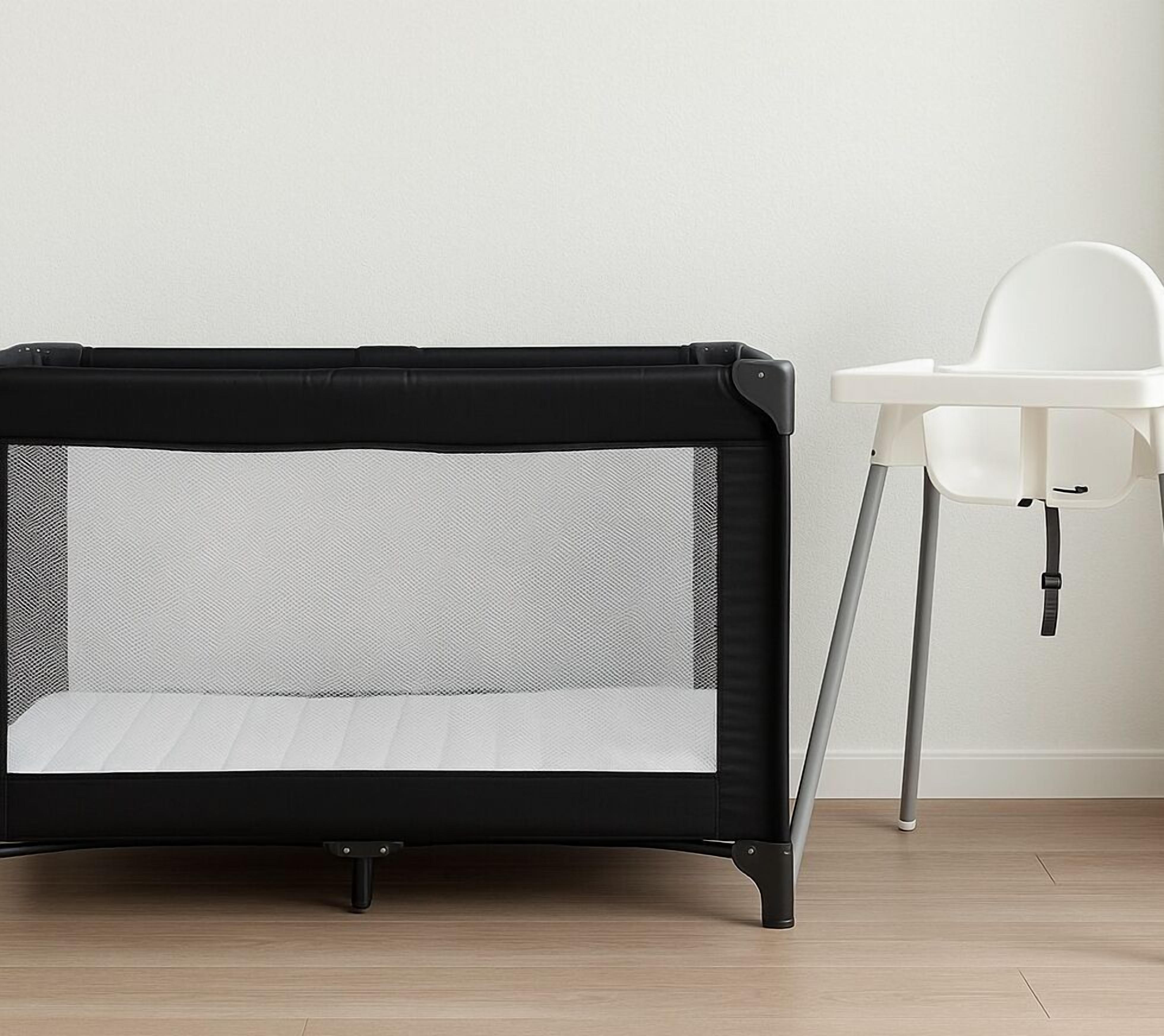 A portable crib with a mesh side and a solid mattress, positioned next to a white high chair.