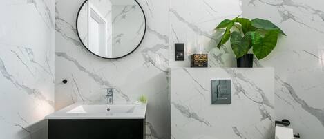 Un baño moderno con lavamanos blanco, tocador negro y un espejo grande.