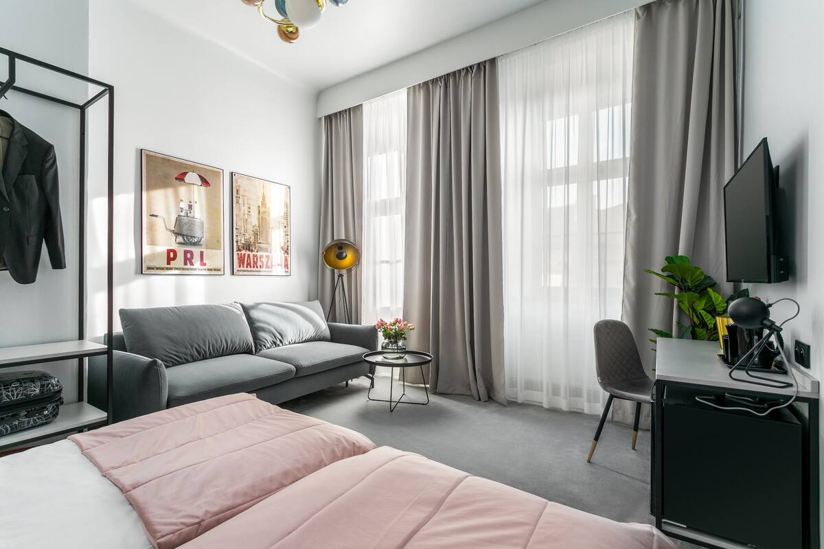 Ein modernes Hotelzimmer mit Bett, Sofa, Schreibtisch, Stuhl, Fernseher und einem Fenster mit Vorhängen.