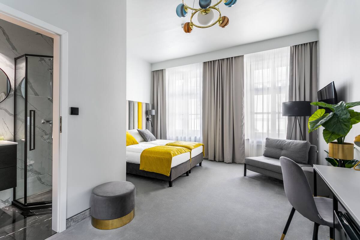 Ein modernes Hotelzimmer mit Bett, Schreibtisch, Stuhl, einer großen Pflanze und einer Dusche.