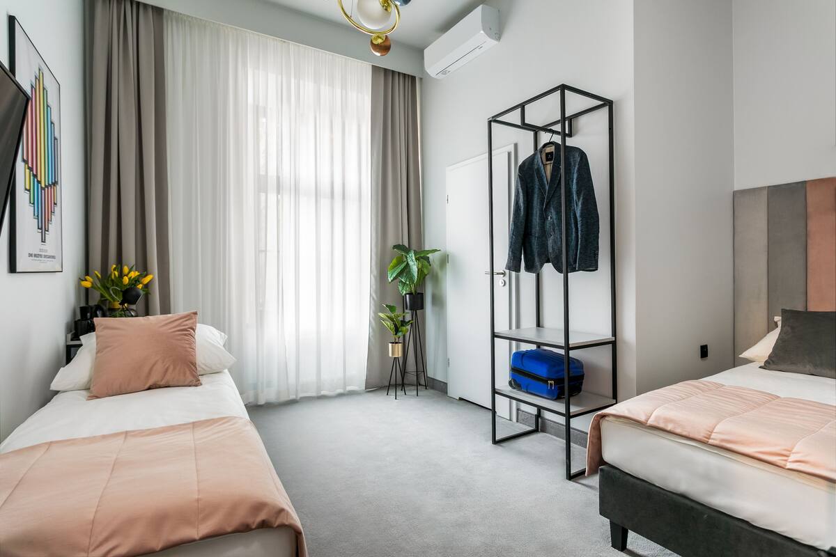 Ein modernes Hotelzimmer mit zwei Betten, einem Kleiderschrank, einer Pflanze und einem Bild an der Wand.