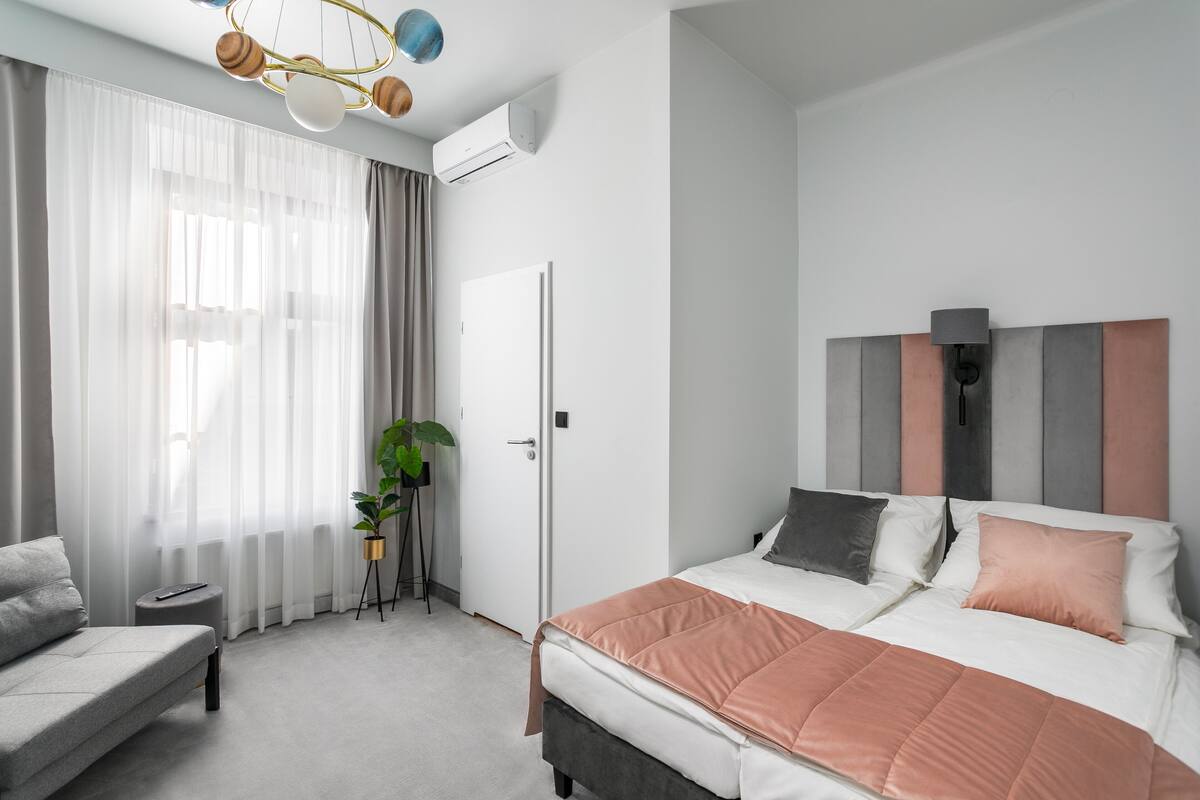 Ein modernes Schlafzimmer mit Bett, Sofa, einem kleinen Tisch, einer Topfpflanze und einer Klimaanlage.