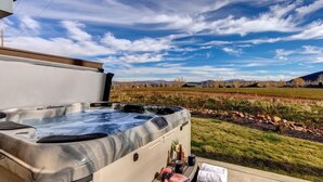 A hot tub with a view of a grassy field and mountains.