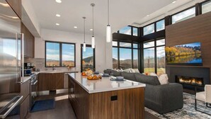A modern kitchen with a central island, a dining area with a view, and a living room with a fireplace.