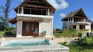 Uma casa de dois andares com piscina, área de estar externa e telhado de palha.