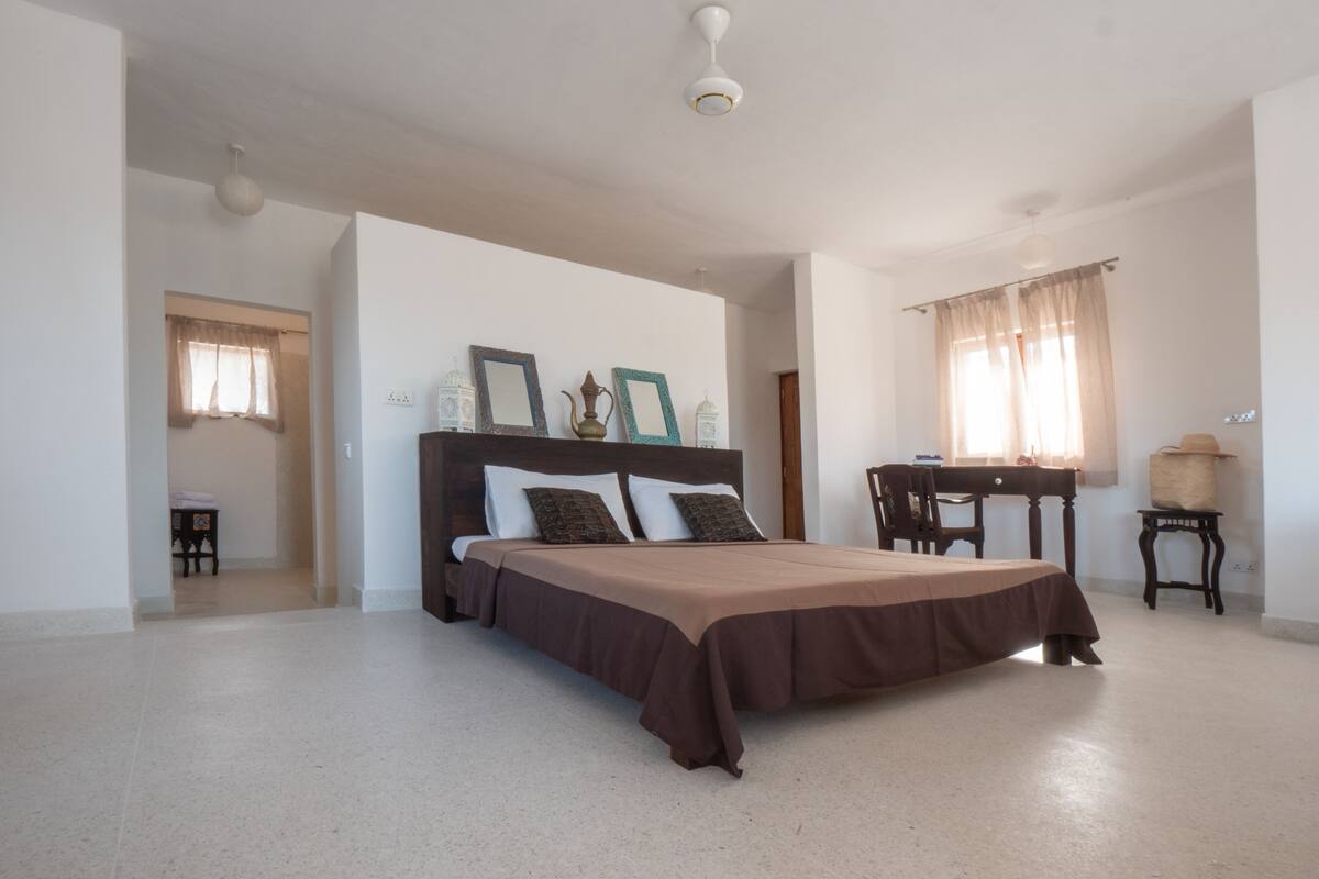 Un dormitorio con cama, escritorio, silla y ventana con cortinas.