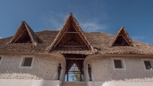 Um edifício com telhado de palha, paredes brancas e uma escadaria que leva à entrada.