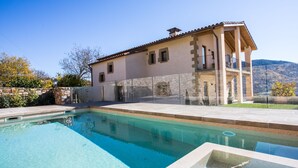 A poolside view of a house with a stone facade, a balcony, and a clear blue pool.