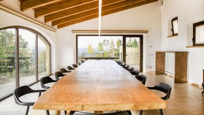 A conference room with a long wooden table, black chairs, and large windows offering a view of trees and a building.