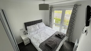 A bedroom with a bed, bedside table, and a window with curtains. - Cosy 2 Bedroom Lodge with onsite Pool (Oulton Broad, Lowestoft)