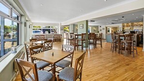 A spacious dining area with wooden tables and chairs, a bar area with shelves of bottles, and large windows providing natural light. - Cosy 2 Bedroom Lodge with onsite Pool (Oulton Broad, Lowestoft)
