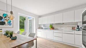 Una cocina moderna con armarios blancos, una mesa de comedor de madera y vistas a zonas verdes.