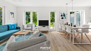 Una sala de estar moderna con un sofá azul, un sofá gris y un comedor con sillas blancas y una mesa de madera.