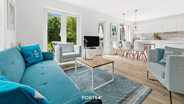 Una sala de estar moderna con sofá, mesa de centro y televisor. Hay un comedor con sillas y una mesa.